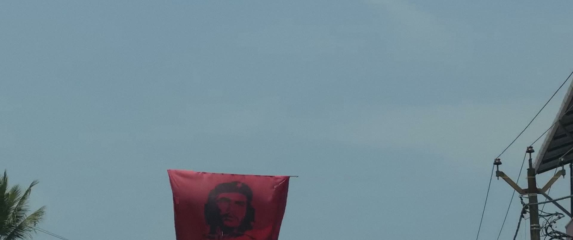 A red flag bearing a portrait flies against a pale evening sky.