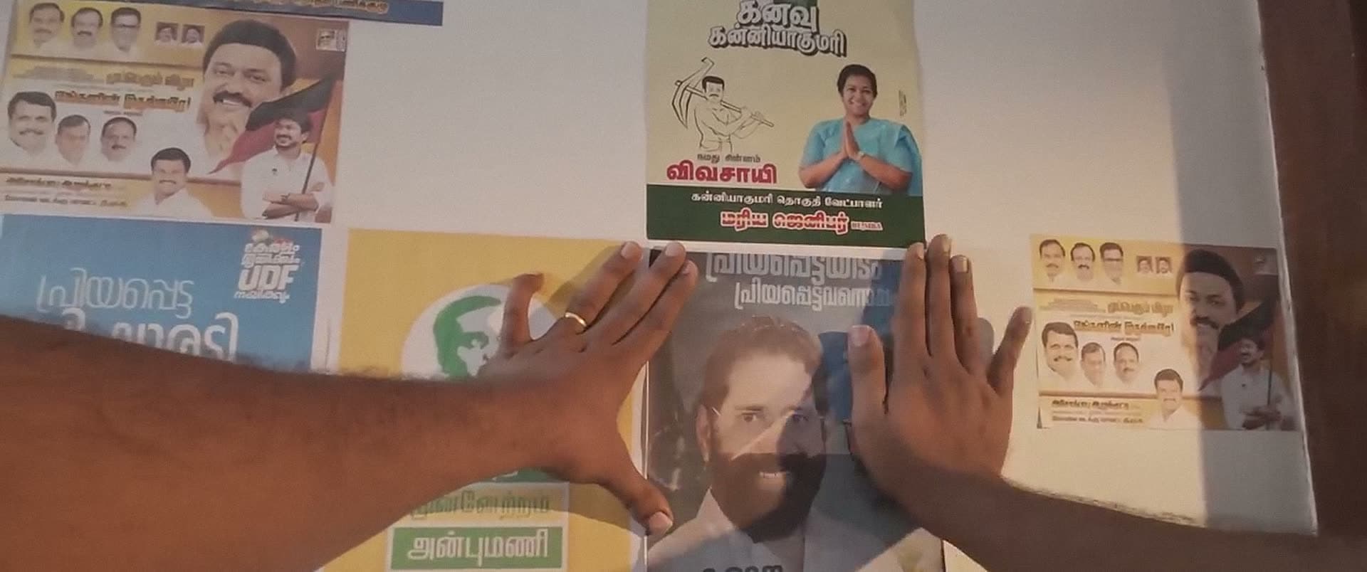 Two hands press a new poster onto a wall already layered with others.