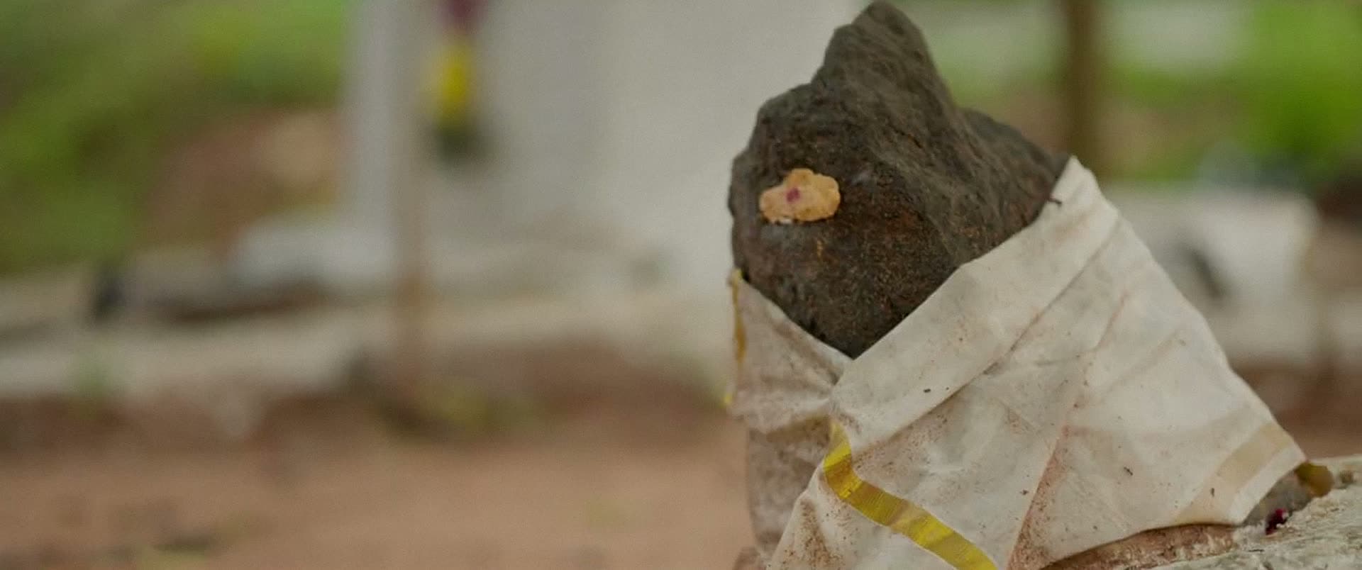 A rough stone wrapped in white cloth, with a dab of colour pressed onto it.