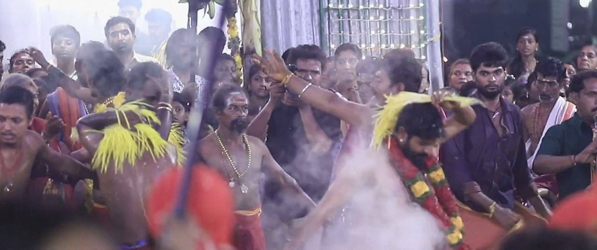 A dense festival crowd, with dancers moving through a cloud of smoke.