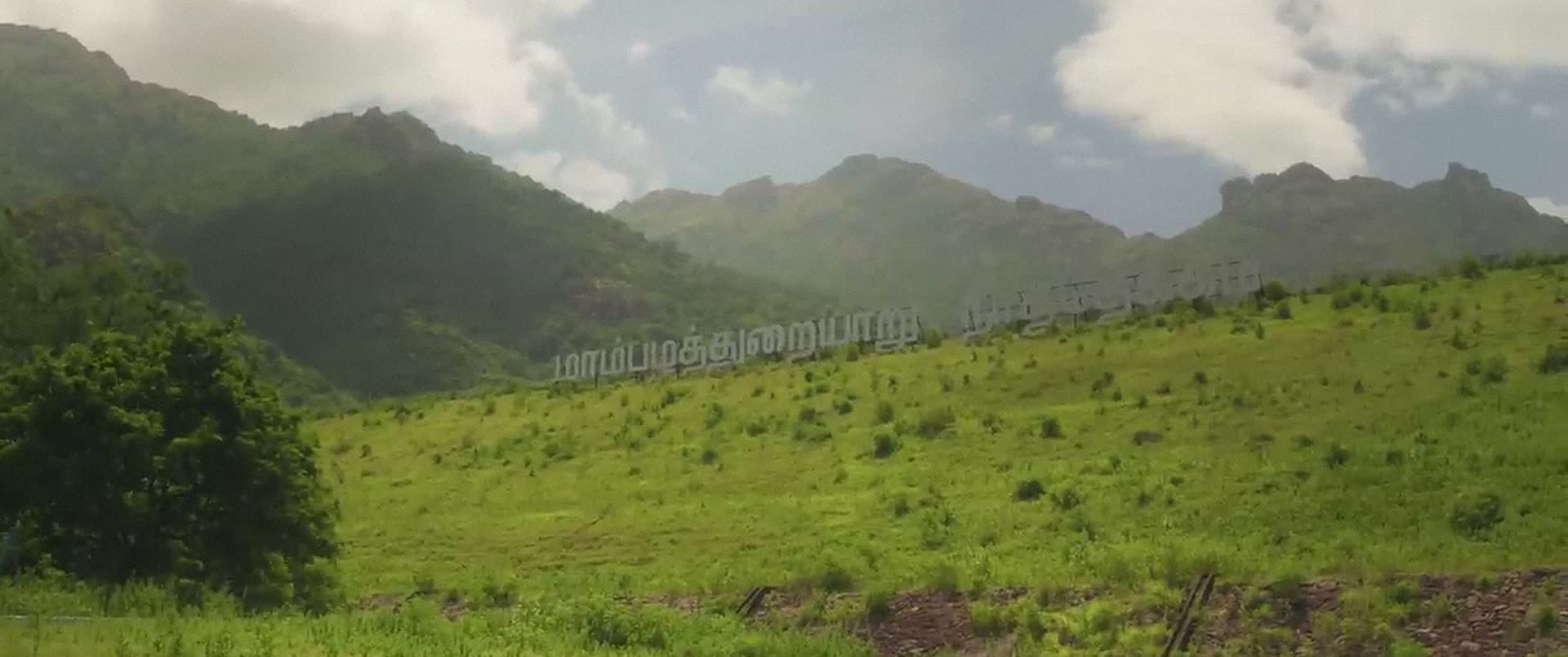 Rolling green slopes rising towards cloud-covered mountains.